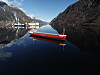 Rött lastfartyg på spegelblank fjord mellan höga berg en klar dag