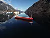 Rött lastfartyg på spegelblank fjord mellan höga berg en klar dag