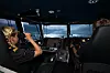 Två personer på en kommandobrygga med instrument och utsikt mot havet.