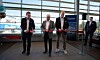Fyra män står framför en röd invigningsbanderoll i en ljus terminal med stora fönster mot hamnen.