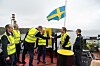 Personer i varselvästar hissar en svensk flagga på ett fartygsdäck i hamn.