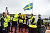Personer i varselvästar hissar en svensk flagga på ett fartygsdäck i hamn.
