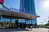 Exteriör av Svenska Mässan i Göteborg med glasfasad, flaggstänger och en person som går framför entrén.