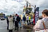 Flera personer står på en landgång och går ombord på en gul bogserbåt vid kajen.