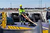 Hamnarbetare i gul skyddsutrustning arbetar med slangar på ett fartygsdäck.