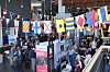 Många människor samlas i en mässhall under hängande internationella flaggor.