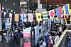 Många människor samlas i en mässhall under hängande internationella flaggor.