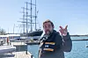 Johnny Sid på en kaj med segelfartyget Pommern och hamnvatten i bakgrunden.