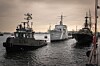 Tre örlogsfartyg förtöjda i en hamn vid vattenytan under en molnig himmel.