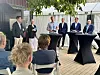 Fem personer deltar i en paneldiskussion utomhus med publik sittande framför.